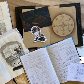 Skizzenbücher und Notizbücher auf dem Boden mit verschiedenen Ständen der "Hutmacherin" und dem neuen Projekt.